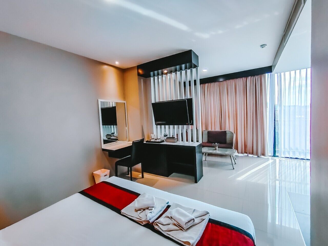 Habitación de hotel moderna con una cama grande, un escritorio, un televisor de pantalla plana y una zona de estar con cortinas.