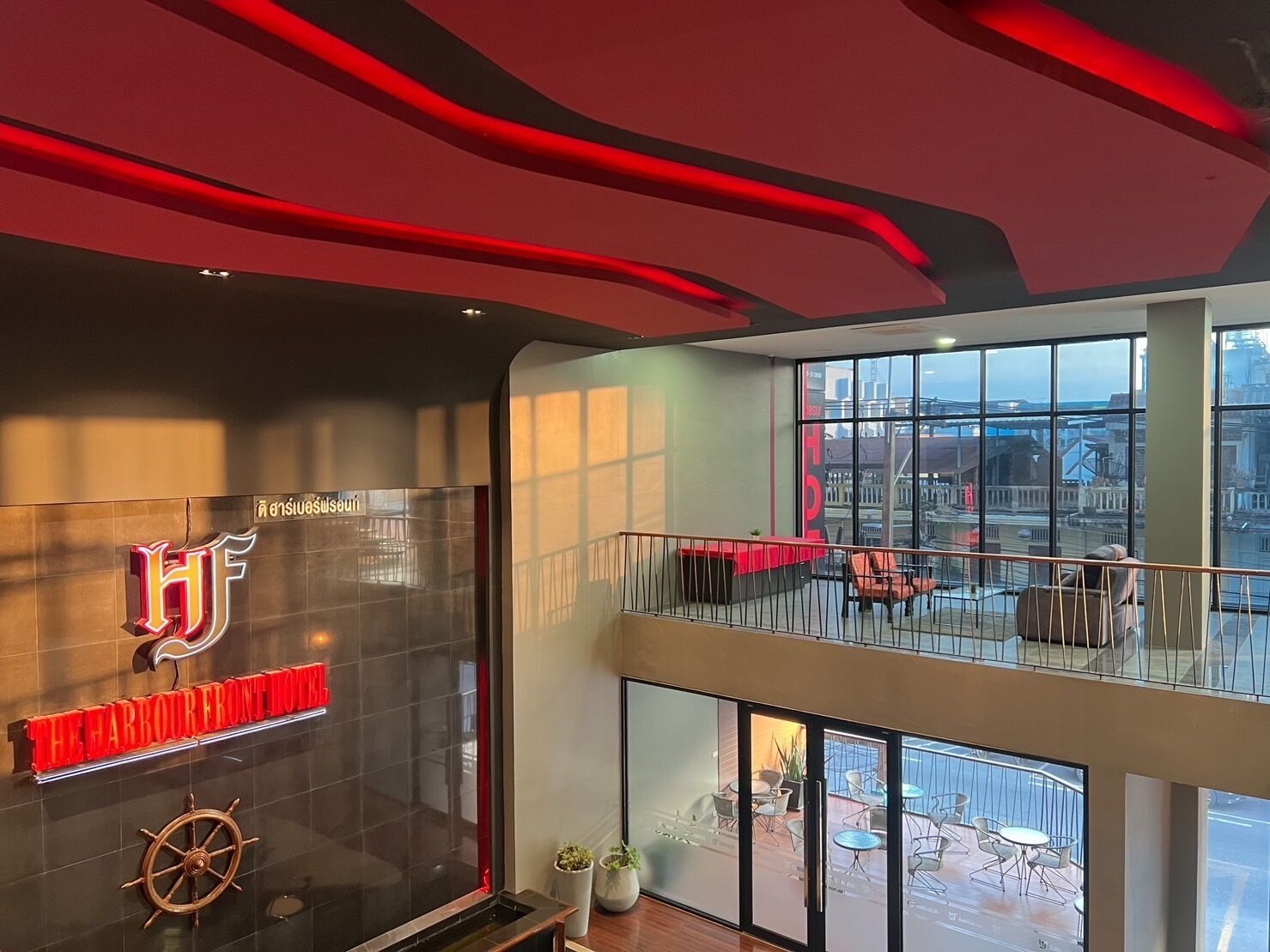 Un intérieur d’hôtel moderne, avec une enseigne bien visible indiquant « Harbour Front Hotel », une grande fenêtre offrant une vue sur la ville et un balcon avec des sièges d’extérieur.