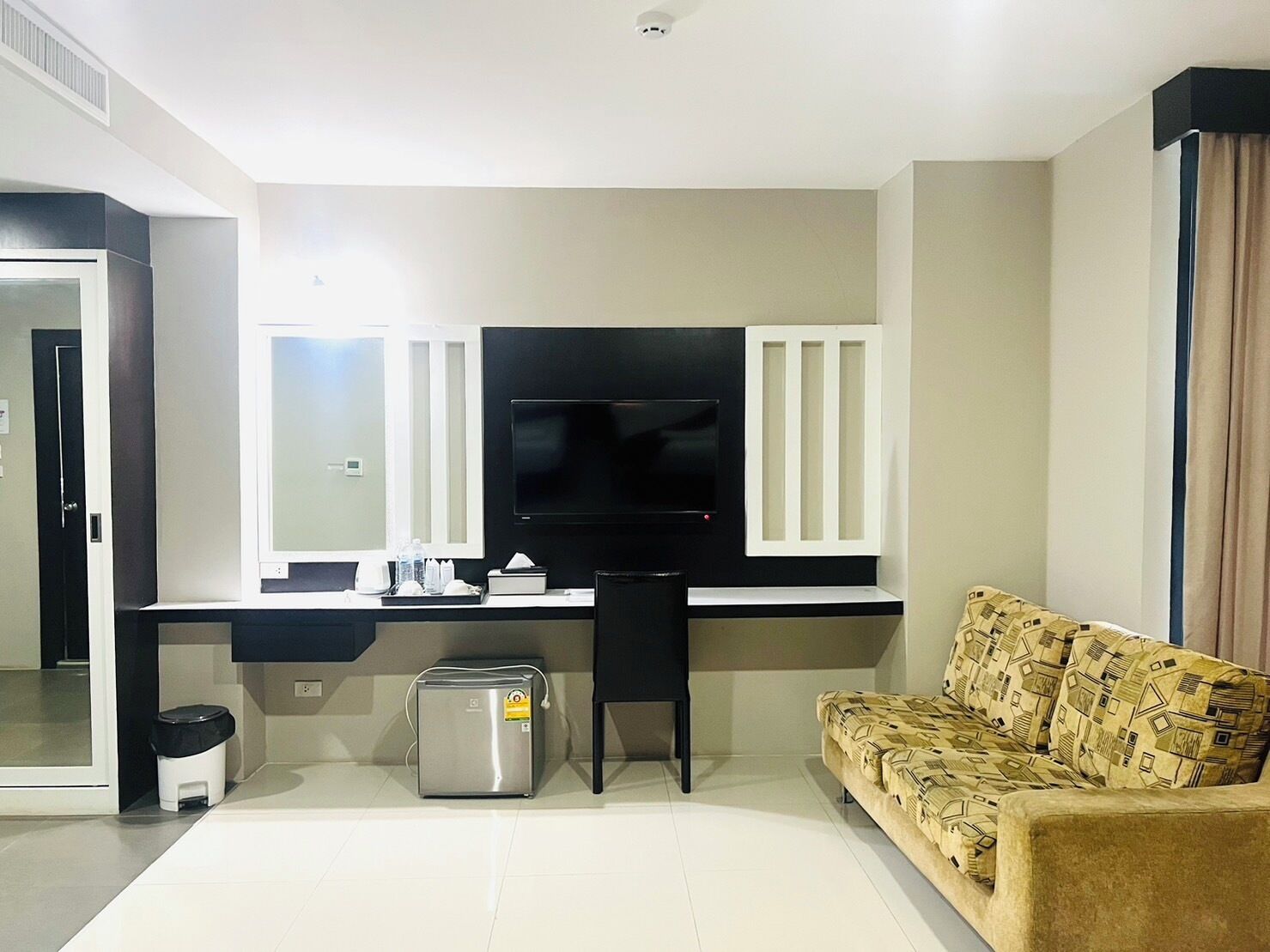 A modern living room with a flat-screen TV, a sofa, and a small trash bin.