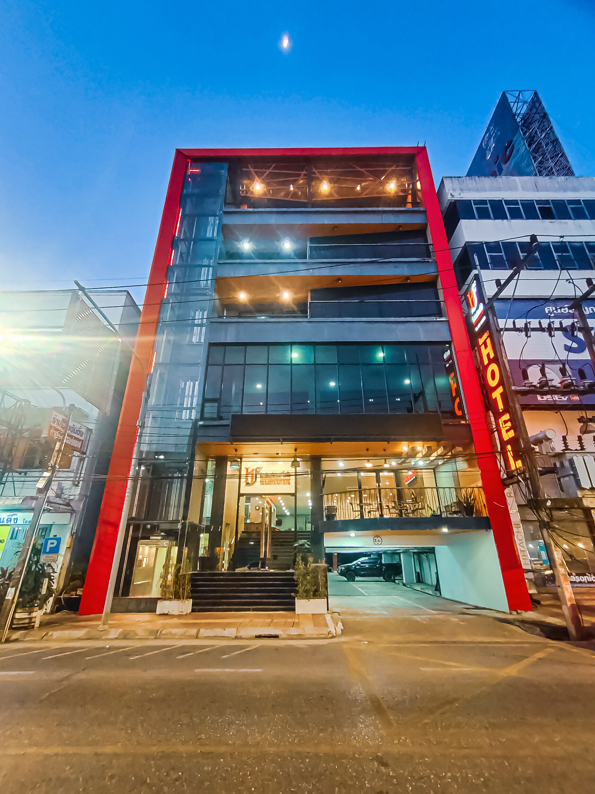 A modern hotel with a red and black facade, multiple floors, and a visible entrance with steps leading up to it.