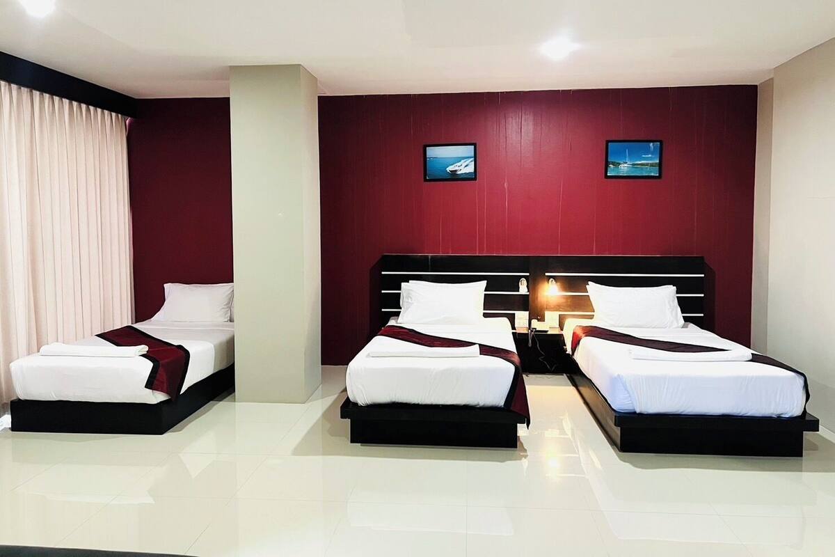 Habitación de hotel con dos camas individuales, un ventanal grande con cortinas y dos televisores empotrados.