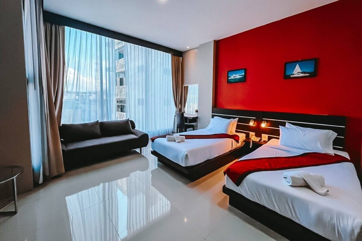 Habitación de hotel con dos camas, un sofá, un escritorio y vistas a la ciudad.