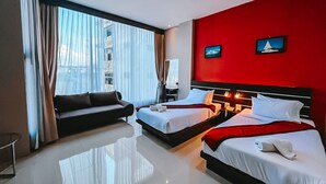 Hotellihuone, jossa on kaksi sänkyä, sohva, työpöytä ja näkymä kaupunkiin.