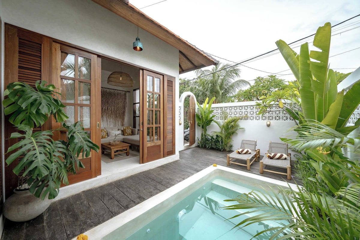 A poolside area with a wooden deck, lounge chairs, and a small seating area with cushions.