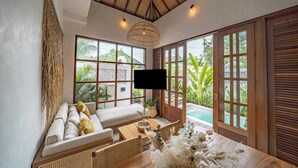 Een ruime kamer met een groot raam, houten plafond, een bank, een eettafel en een televisie.