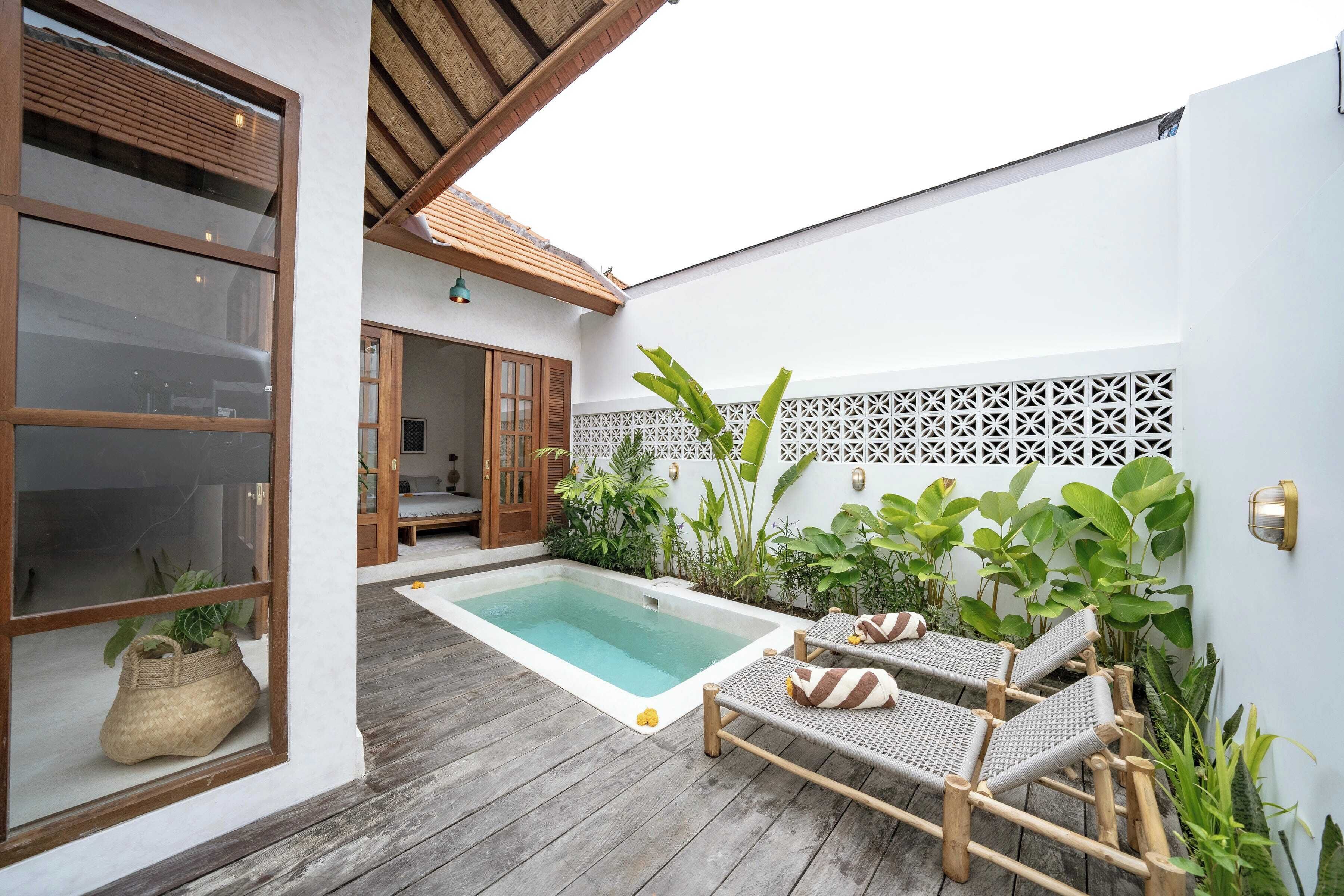 A pool area with lounge chairs, a wooden deck, and a white wall with a decorative lattice.