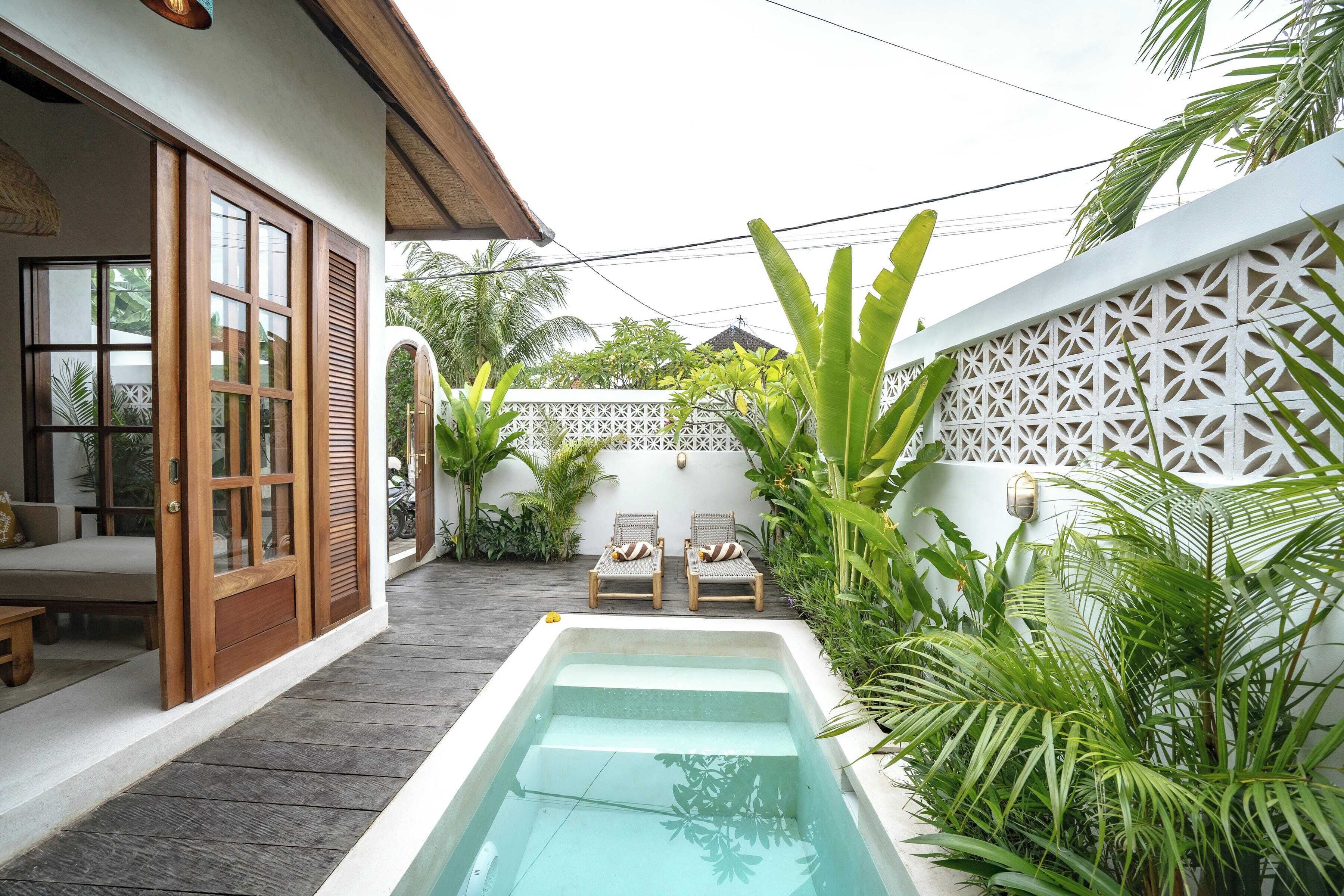 A pool area with wooden deck, two lounge chairs, and a white wall with a geometric pattern.