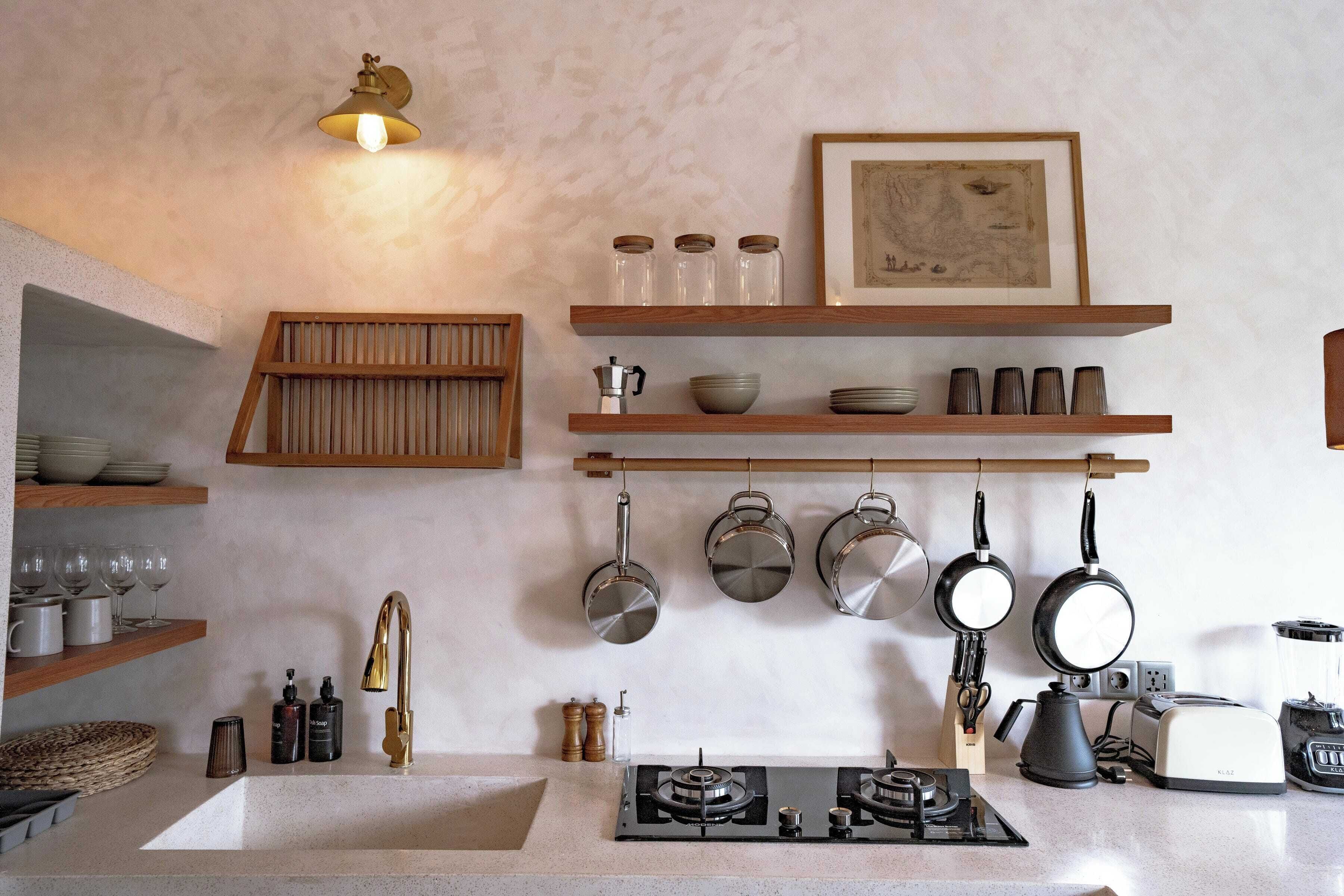 A kitchen with a gas stove, hanging pots, a coffee maker, and wooden shelves with glass jars and bowls.