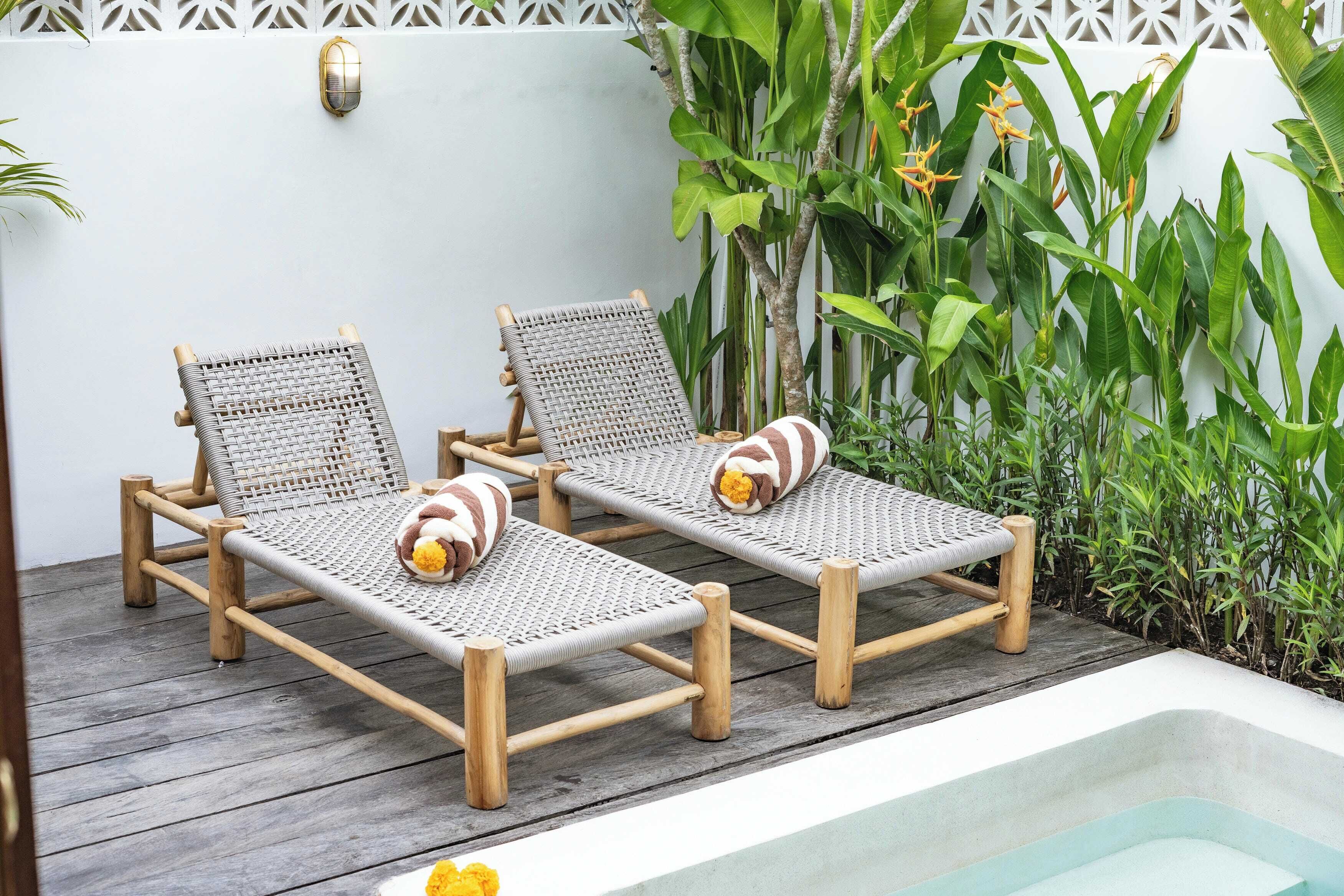 Dos sillones de mimbre con cojines, una piscina pequeña y exuberante vegetación al fondo.