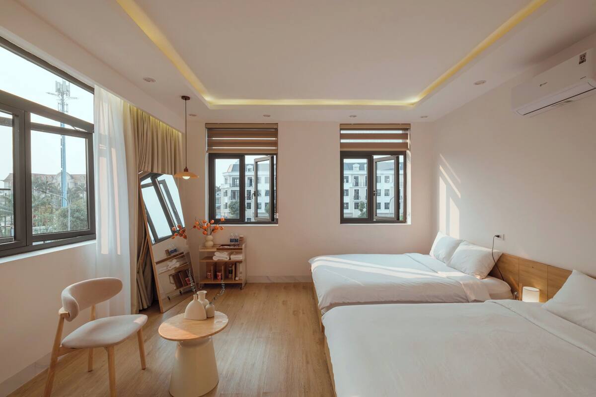Quarto de hotel com duas camas, uma escrivaninha, uma cadeira e uma mesinha.