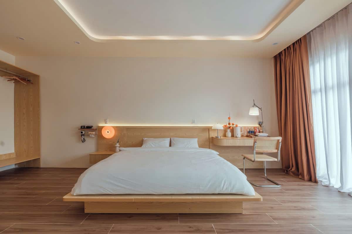 Quarto de hotel moderno com uma cama grande, cabeceira de madeira, mesas de cabeceira e uma janela com cortinas.