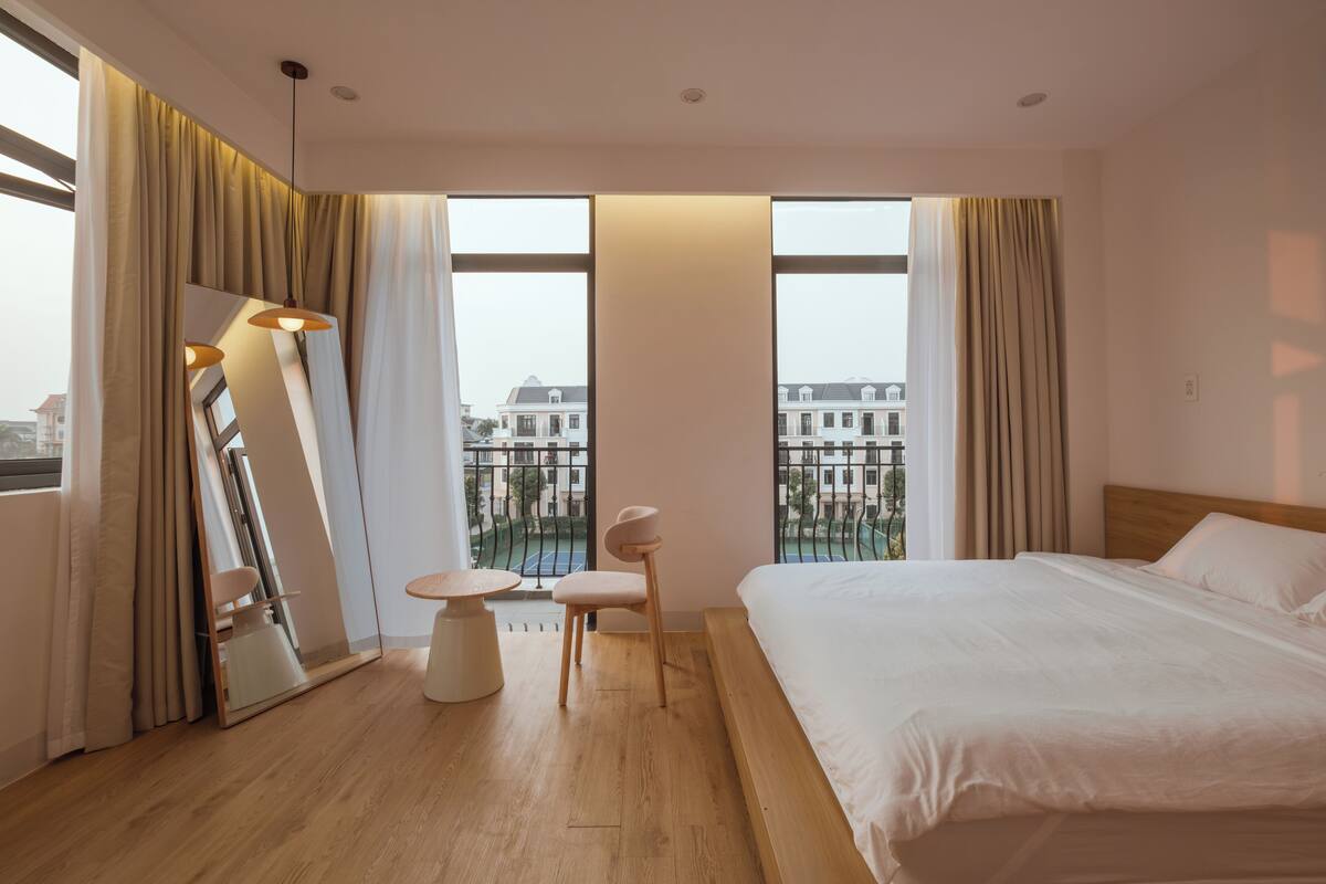 Quarto de hotel moderno com uma cama grande, uma mesa redonda, uma cadeira e um espelho.