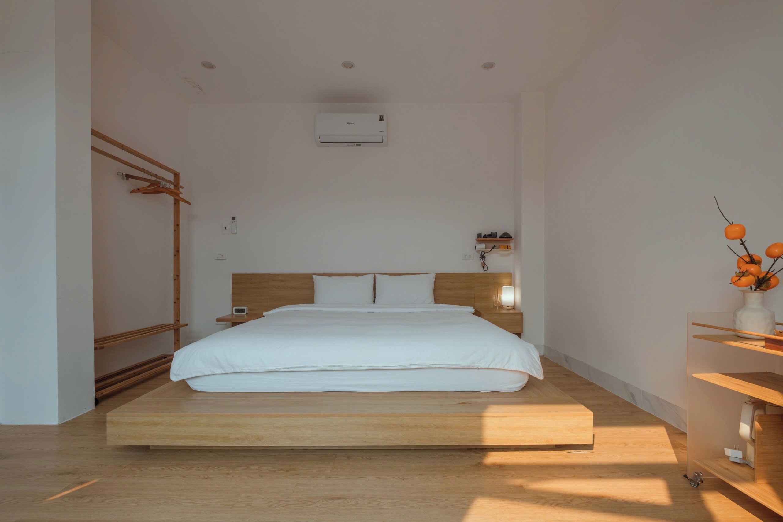 Un dormitorio minimalista con una cama plataforma de madera, una mesita de noche con lámpara y un aire acondicionado instalado en la pared.
