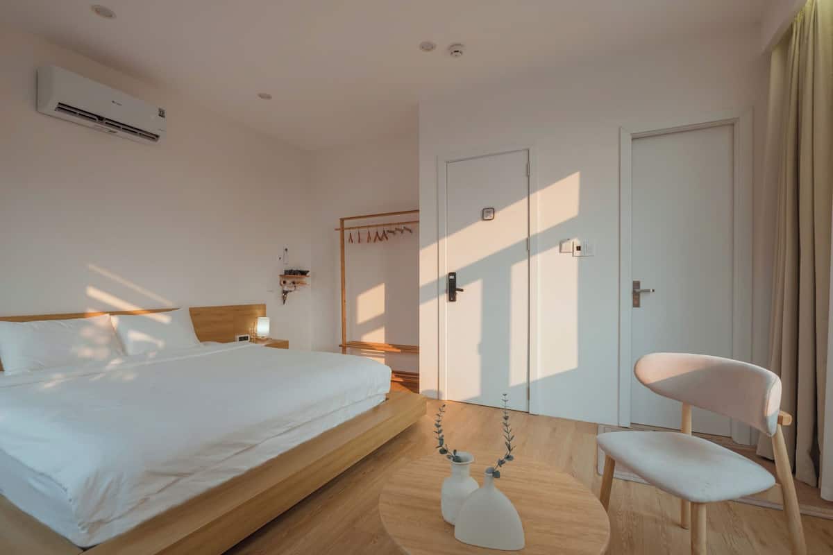 Quarto de hotel com cama, mesa de cabeceira, luminária, guarda-roupa e uma cadeira.