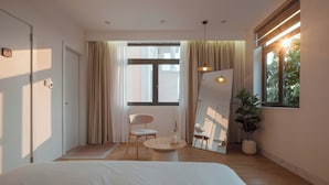 A modern bedroom with a large bed, a round wooden table, a chair, and a potted plant.