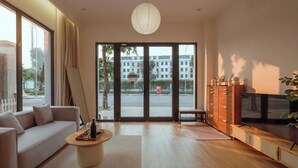 Una sala de estar moderna con un sofá, una mesa de centro, televisión y vistas a la calle a través de amplios ventanales.