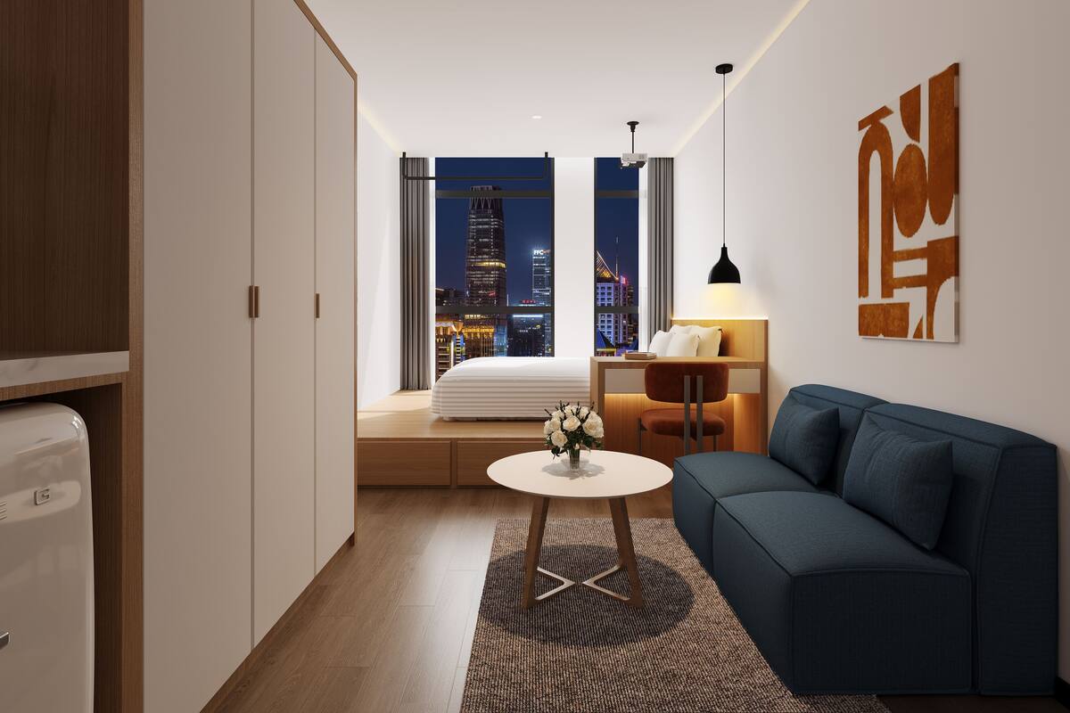 Een moderne hotelkamer met uitzicht over de stad, een bank, een kleine tafel en een lamp.