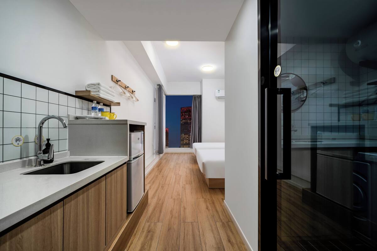 Een compacte hotelkamer met kitchenette, een bed en uitzicht op een stadsgezicht.