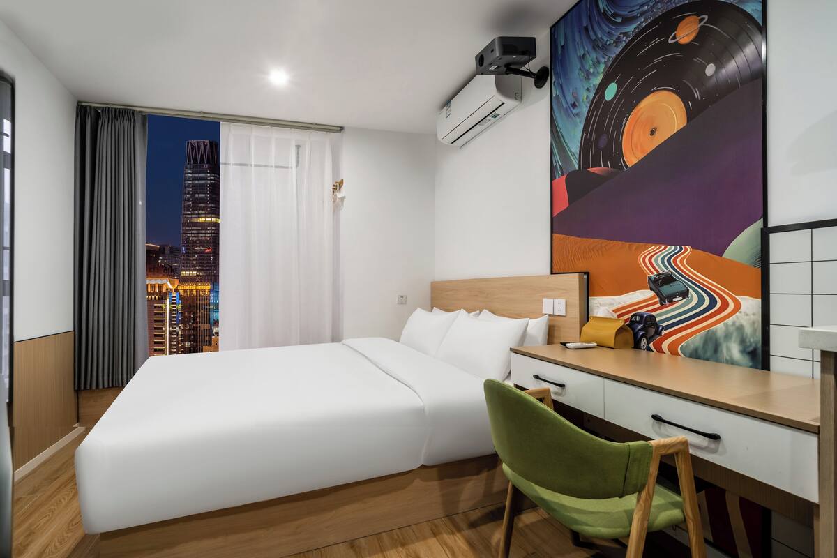 Hotelkamer met een bed, bureau, stoel, airconditioning en uitzicht op de stad.