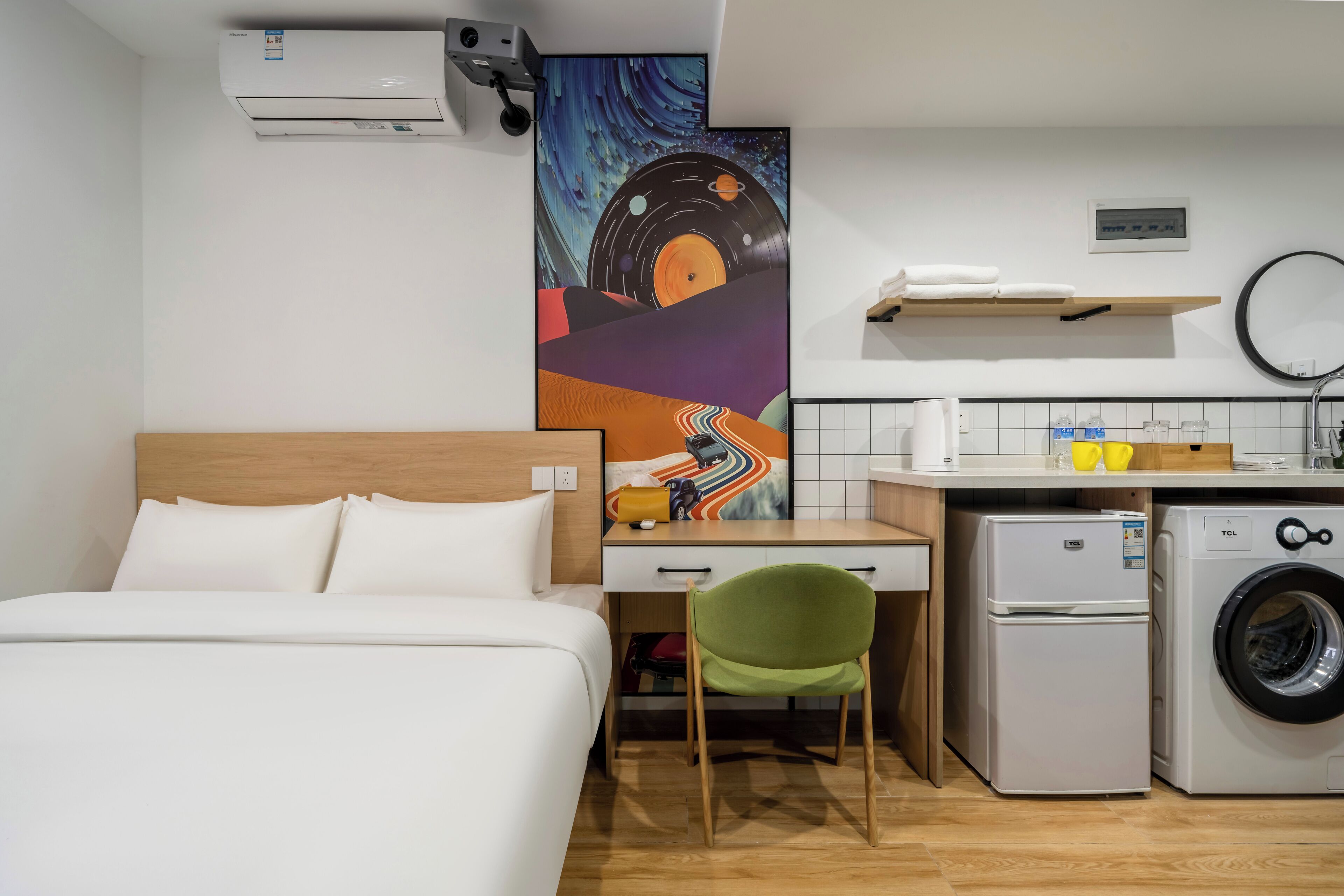 Quarto de hotel com cama, escrivaninha, cadeira, máquina de lavar e ar condicionado fixado na parede.
