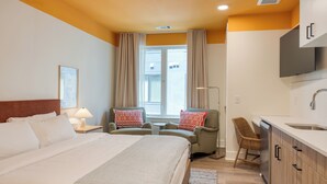 A hotel room with a bed, two armchairs, a desk, a chair, a sink, and a window. - BRAND NEW 4 Deluxe Studios w/ Balcony in 12 South (Nashville)