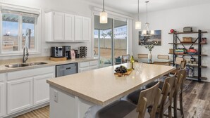 Une cuisine moderne avec des meubles blancs, un grand îlot central et un coin repas doté de chaises en bois.