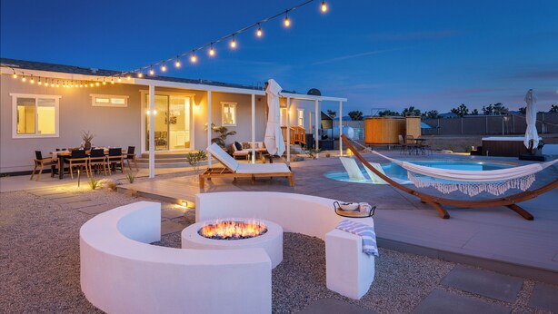 Un espace de vie extérieur moderne comprenant une piscine, des chaises longues et un foyer.