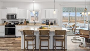 Une cuisine moderne avec des meubles blancs, des appareils en acier inoxydable et un grand îlot central doté de tabourets.