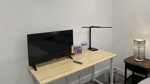 A room with a wooden desk, a flat-screen TV, a desk lamp, a remote control, a water bottle, a box, and a decorative lantern.
