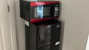 A compact black and red microwave and refrigerator unit in a corner of a room with a white door and wooden flooring.