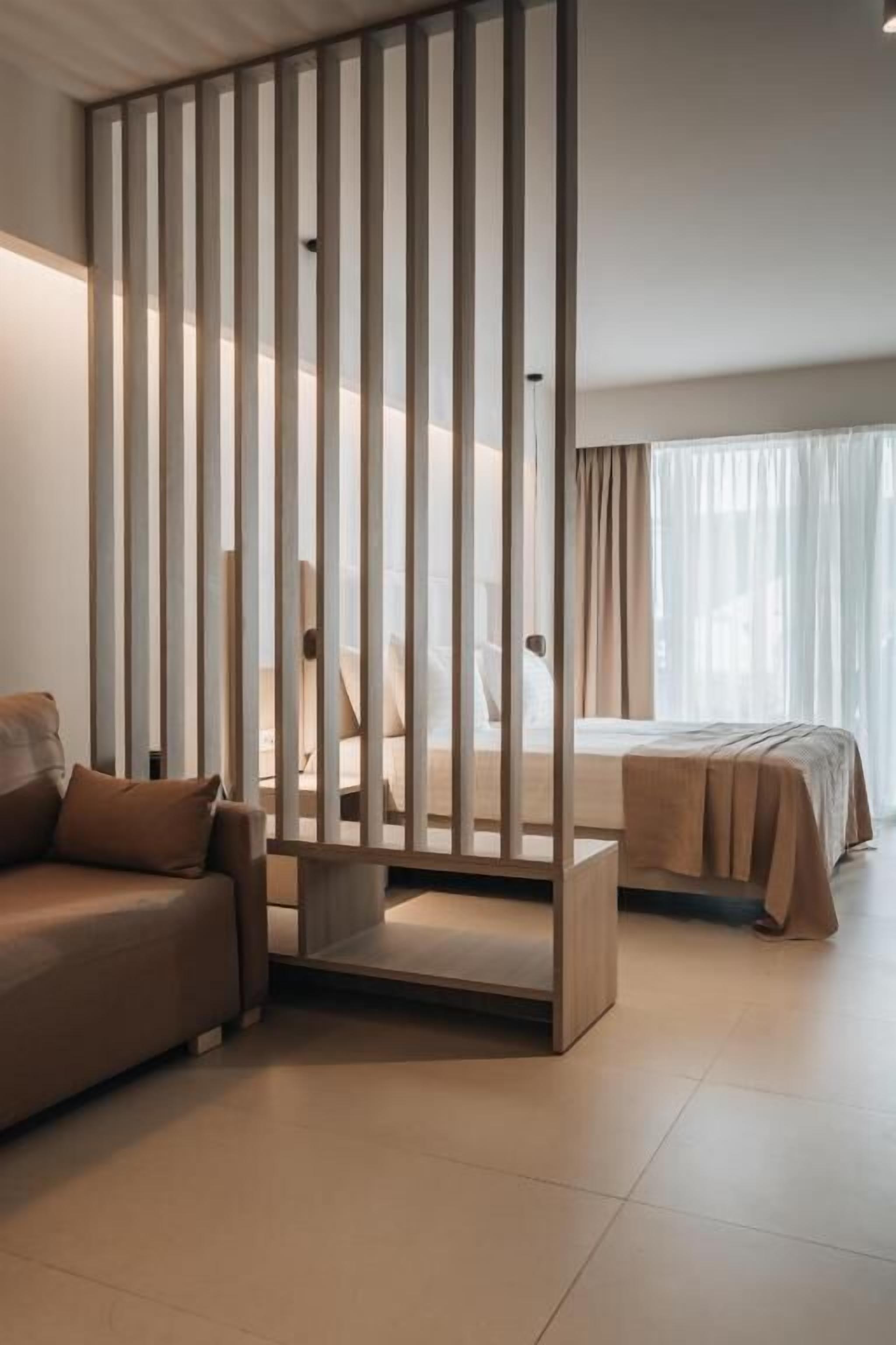 A modern hotel room with a large bed, a sofa, and a partition with vertical slats.