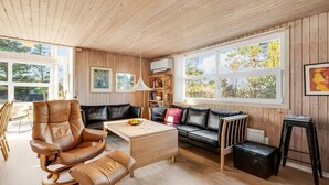 Un vaste espace de vie comprenant un canapé en cuir, une table basse en bois et une table à manger. De grandes fenêtres laissent entrer la lumière naturelle et offrent une vue sur l’extérieur.