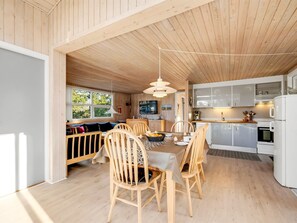 Un intérieur en bois comprenant un coin repas, une cuisine et une fenêtre donnant sur un espace verdoyant.