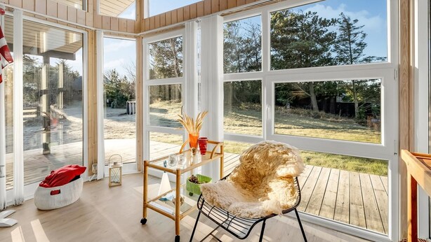 Une pièce spacieuse avec de grandes fenêtres, une terrasse en bois et un coin salon confortable avec un fauteuil et une table.