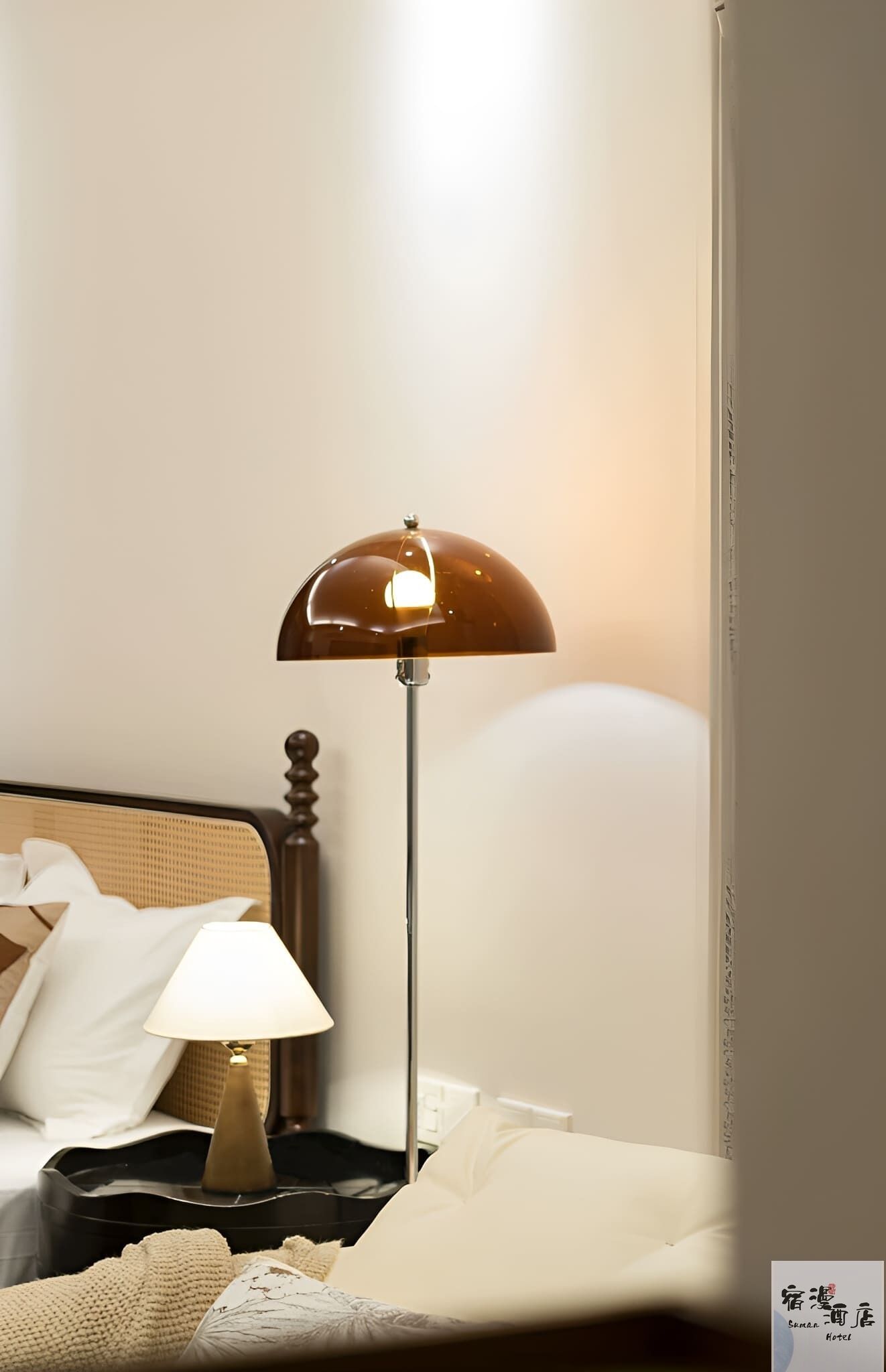 A hotel room with a bed, a nightstand with a lamp, and a wall-mounted lamp.