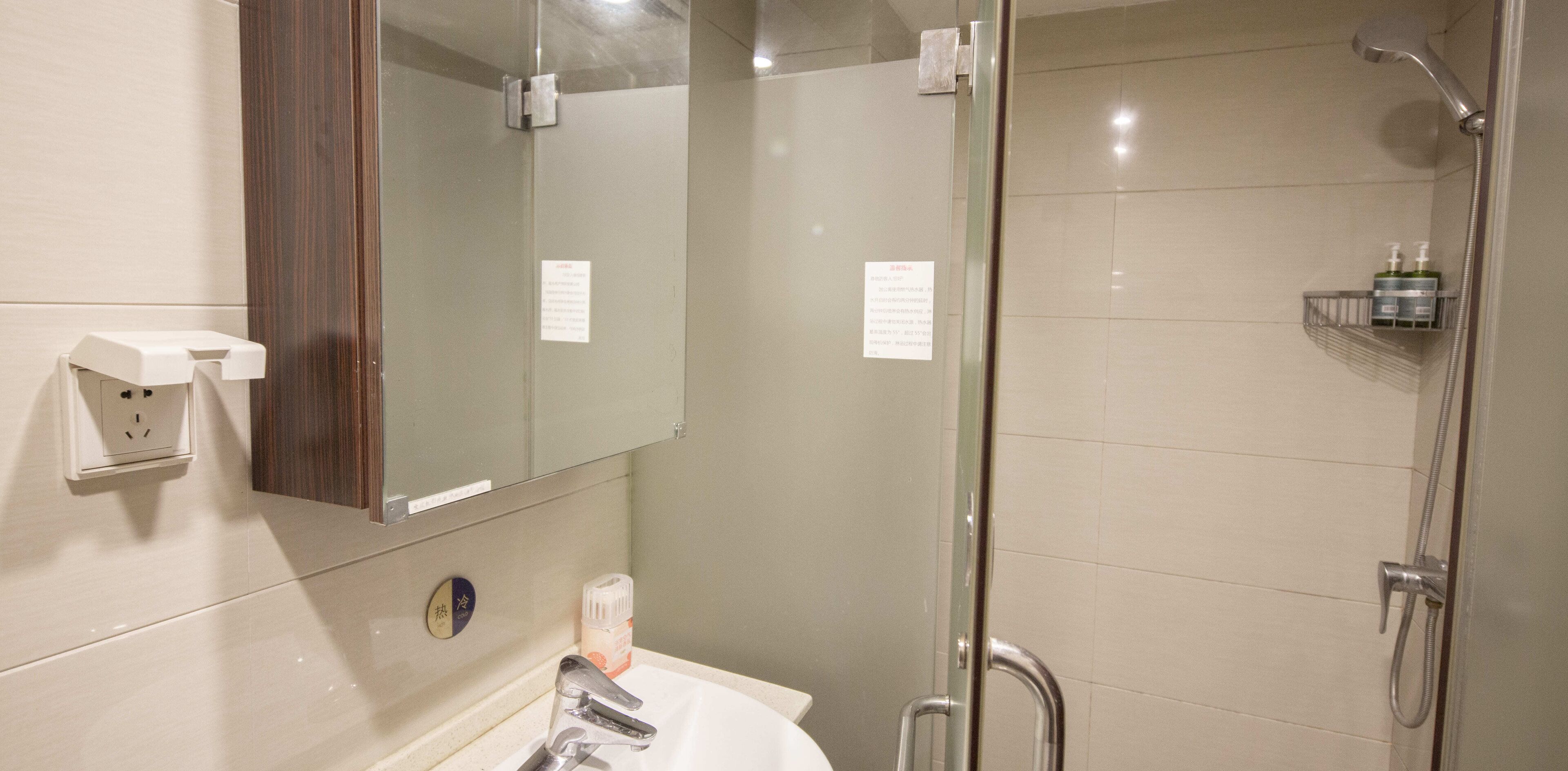 A bathroom with a mirror, a sink, a shower, and a towel rack.