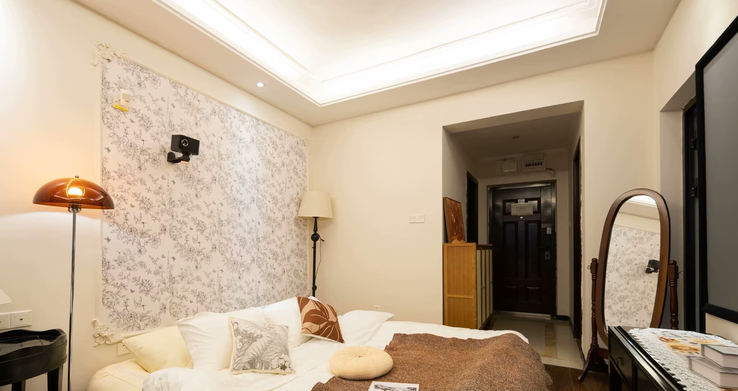 Un dormitorio con cama, mesita de noche, lámpara, espejo y puerta que da a otra habitación.