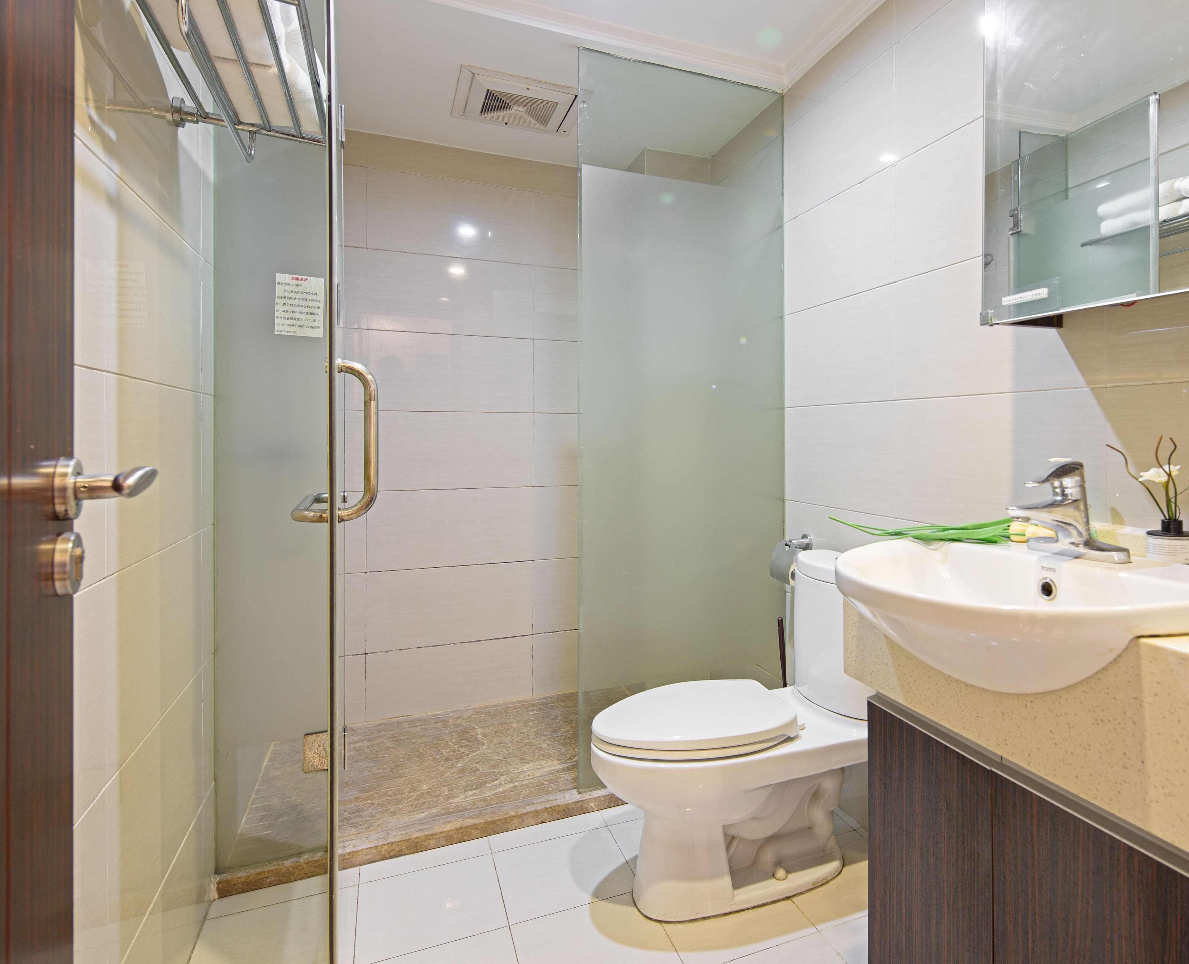 A modern bathroom with a glass shower enclosure, a white toilet, and a sink with a mirror above it.