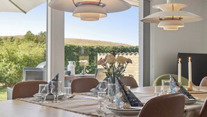 Zona pranzo all'aperto con tavolo apparecchiato per quattro, circondata da sedie, con vista su giardino e colline sullo sfondo.
