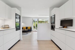 Eine moderne Küche mit weißen Schränken, einem eingebauten Backofen und einem Flachbildfernseher.