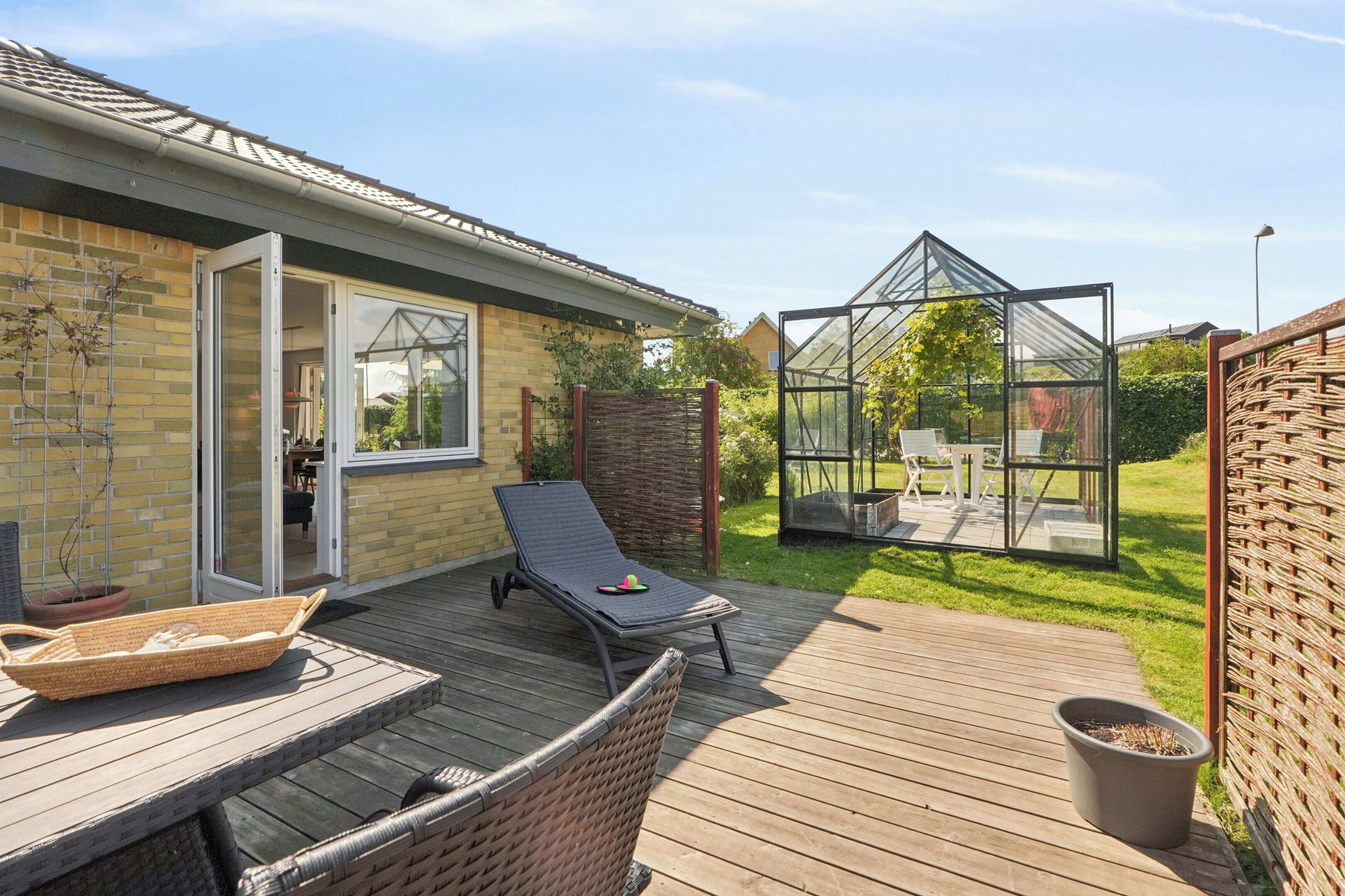 A wooden deck with a glass-enclosed patio area, a wicker chair, and a table with a basket.