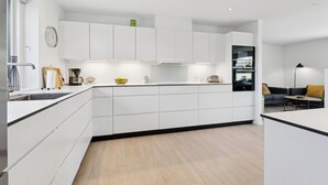 Una cucina moderna con mobili bianchi, forno integrato e zona pranzo con divano e tavolino.