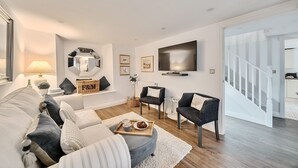Ein modernes Wohnzimmer mit einer Couch, Sesseln, einem Fernseher und einer Treppe.