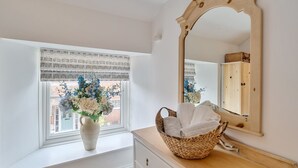 Ein Zimmer mit einem großen Spiegel, einem Fenster mit Blick auf Gebäude, einer Vase mit Blumen und einem Korb mit Handtüchern.