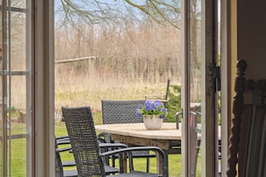 An open door leading to a patio area with a table, chairs, and a potted plant.