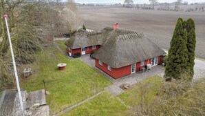 Una propiedad rural con dos casas de campo con techo de paja, un amplio campo abierto y un alto árbol de hoja perenne.