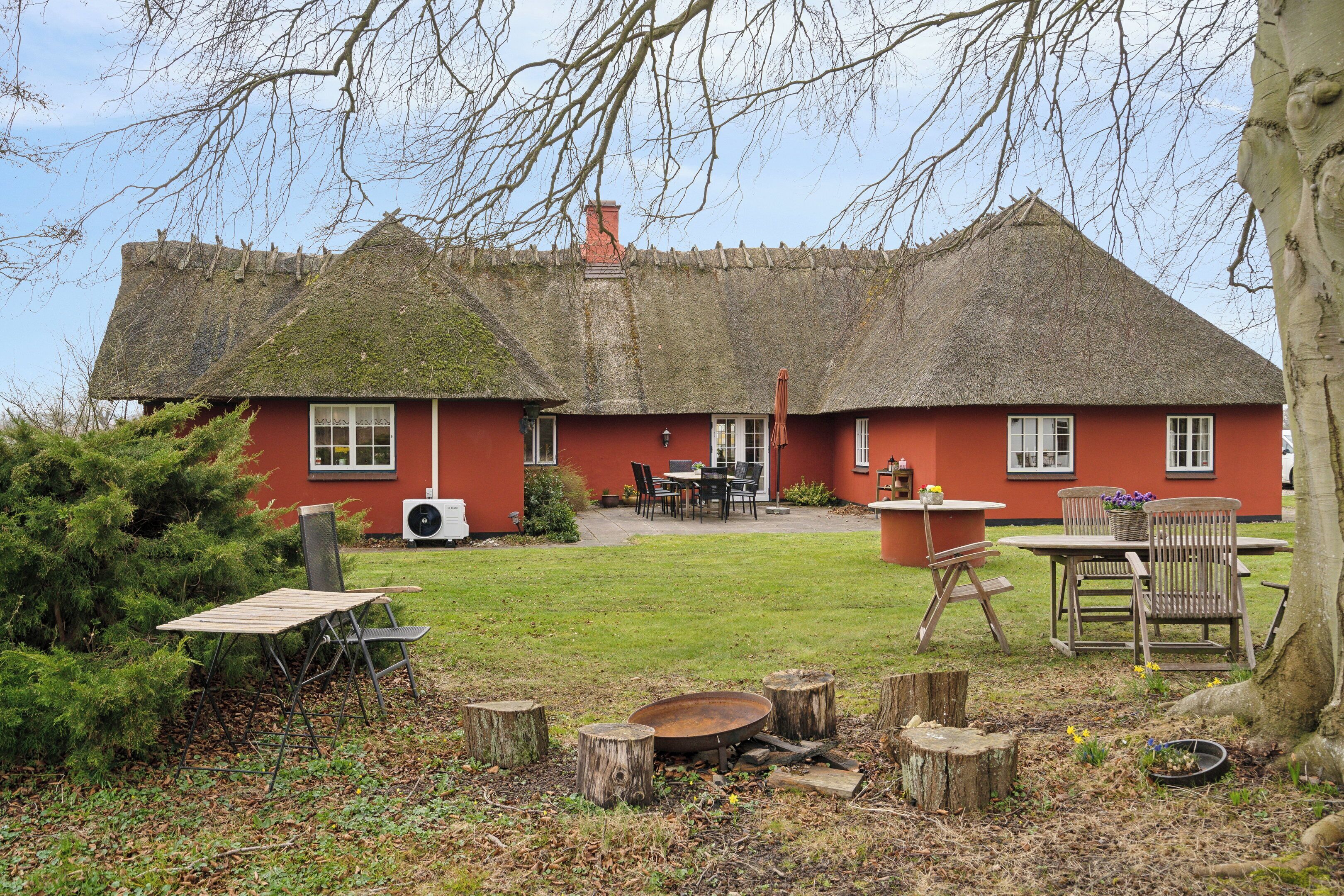 Una casa roja con techo de paja, un patio con muebles de exterior y un jardín.