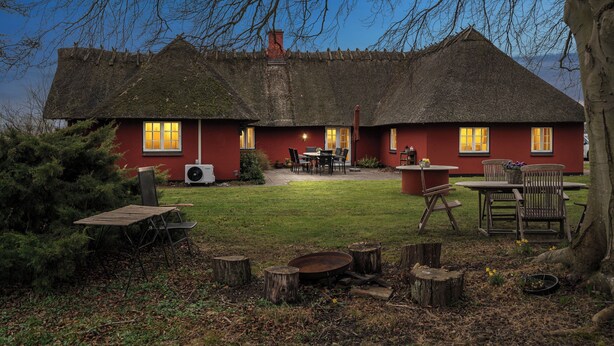 Una casa con techo de paja y fachada roja, un patio con mobiliario exterior y un césped bien cuidado.
