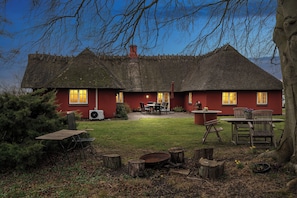 Una casa con techo de paja y fachada roja, un patio con mobiliario exterior y un césped bien cuidado.