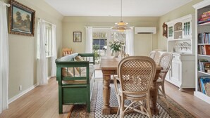 Comedor con mesa de madera, sillas de mimbre, banco verde y estantería blanca.
